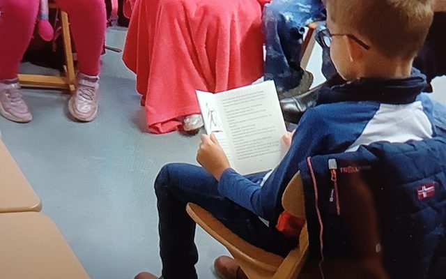 Kinder sitzen im Sitzkreis, ein Kind liest vor.