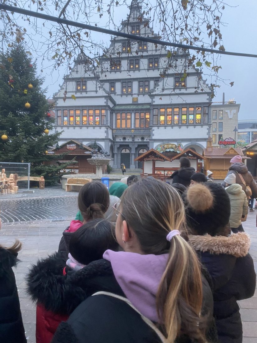 Die Kinder sind auf dem Weg ins Theater. ES ist eine Reihe Kinder von hinten zu sehen. Im Hintergrund das geschmückte Rathaus.