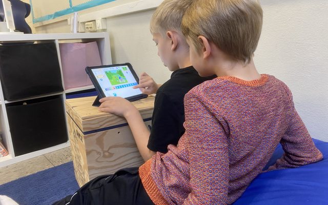 Kinder sitzen gemeinsam auf einem Sitzsack und programmieren am Tablet.