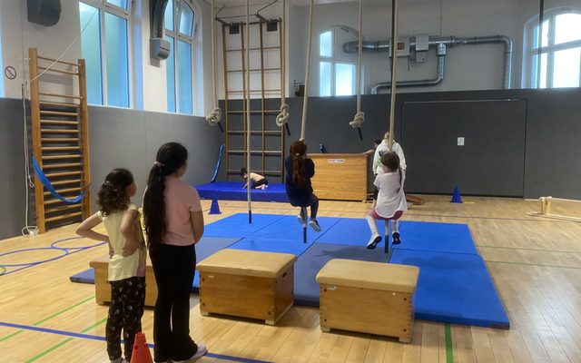 Kinder schwingen an Seilen beim Bewegungsparcours in der Sporthalle.